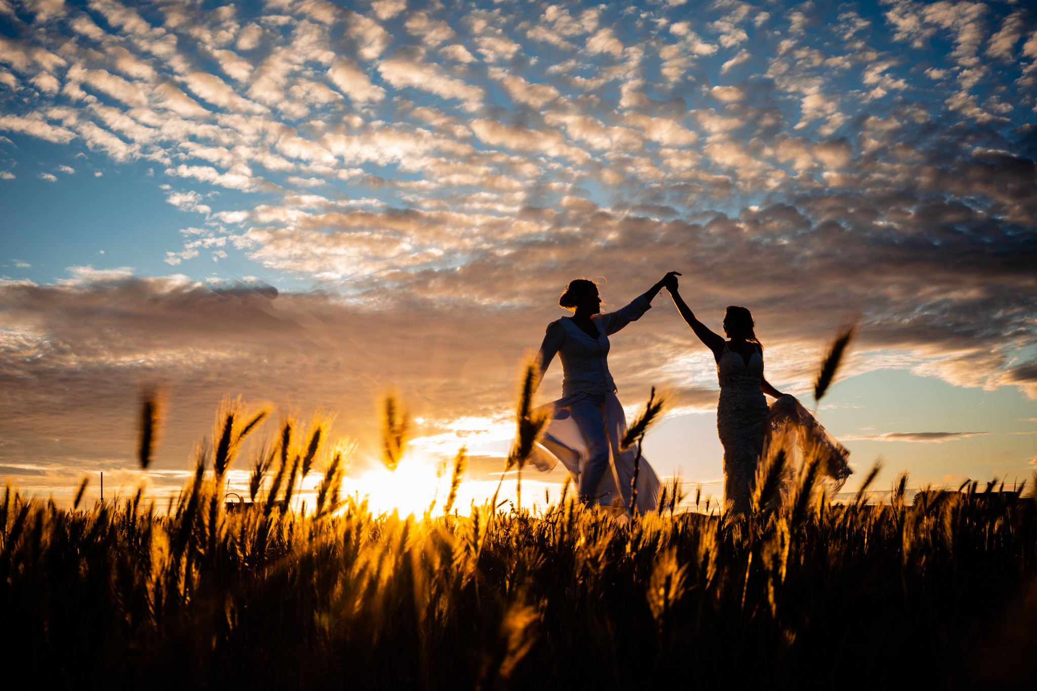 Same sex wedding couple dancing in the sunset. Silhouette of brides in a field of wheat.
